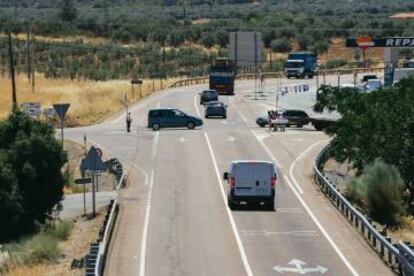 Varios vehículos circulan por la N-435 a la entrada de Almendral, donde los peatones aguardan para cruzar la carretera.