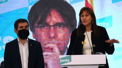 Laura Borràs, acompañada de Jordi Sànchez, frente a una pantalla con el rostro de Carles Puigdemont.