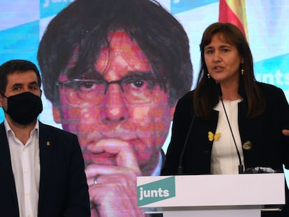 Laura Borràs, acompañada de Jordi Sànchez, frente a una pantalla con el rostro de Carles Puigdemont.