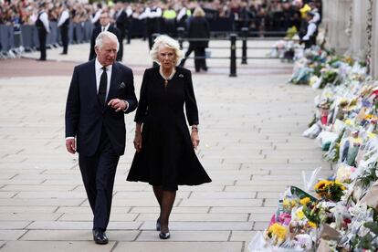 Los reyes Carlos y Camila miran los ramos de flores colocados a las puertas del palacio de Buckingham. 