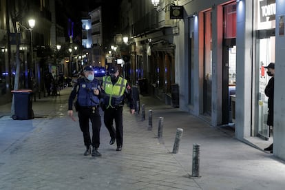 Agentes de policía mantienen este sábado casi vacío uno de los tramos de la céntrica calle madrileña de Espoz y Mina poco antes de que se cumpla el toque de queda.