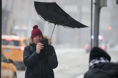 Un turista toma una fotografía mientras intenta sostener el paraguas, en Manhattan, Nueva York.