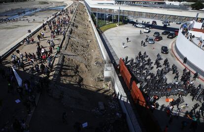 La policía mexicana hace guardia mientras los migrantes caminan por la orilla del río Tijuana, casi seco, mientras se dirigen hacia la puerta de entrada de El Chaparral.