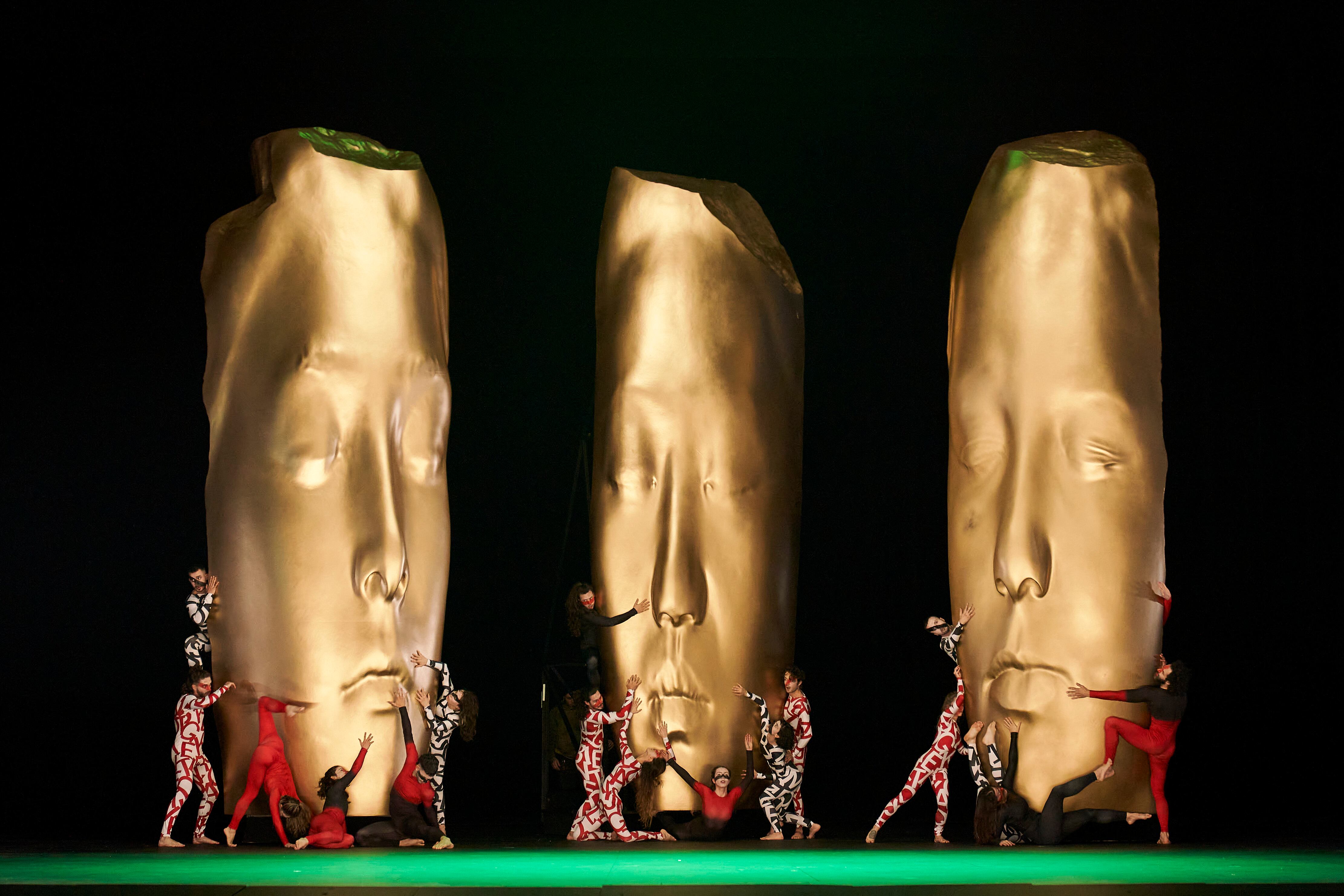 Tres bustos gigantes de color dorado presiden el escenario ante los bailarines en un momento de la ópera. / DAVID RUANO (Liceu)