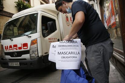 Un empleado municipal coloca un cartel en Ordizia (Gipuzkoa) informando de la obligación de llevar mascarilla.