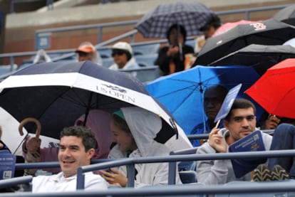 Aficionados se protegen de la lluvia en las gradas de la pista dobe debía jugarse el encuentro entre Nadal y Djokovick.