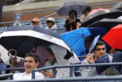 Aficionados se protegen de la lluvia en las gradas de la pista dobe debía jugarse el encuentro entre Nadal y Djokovick.