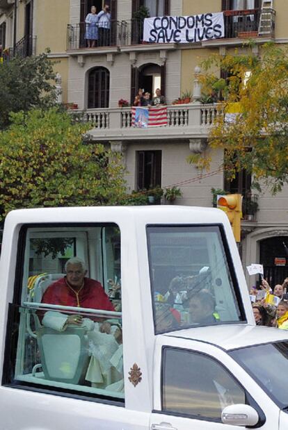 Benedicto XVI, en su <i>papamóvil,</i> pasa bajo una pancarta en inglés en la que reza: "Los condones salvan vidas".