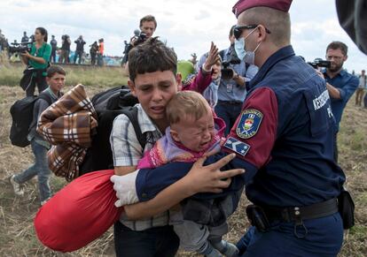 Un policía intenta placar a un niño refugiado que sujeta a un bebé cerca de Röszke (Hungría). Un grupo de unos 150 refugiados ha huido de esta ciudad al sur del país en un intento de evitar ser registrados e identificados por las autoridades, informó la agencia MTI.