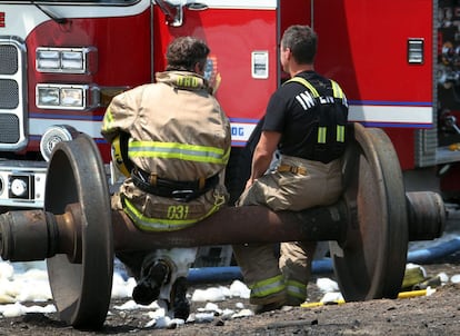 Dos bomberos descansan sobre las ruedas de uno de los vagones del tren cargado de crudo que descarriló en el centro de la ciudad canadiense de Lac-Mégantic.
