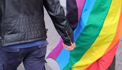 una pareja se coge la mano con la bandera multicolor, en una foto de archivo.