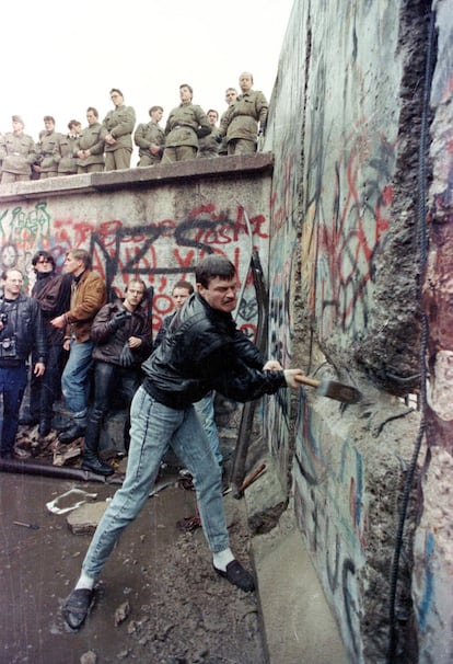 Um manifestante golpeia com um martelo uma das paredes do Muro de Berlim Oriental, enquanto as forças de segurança observam de cima, perto do Portão de Brandemburgo, em 11 de novembro.