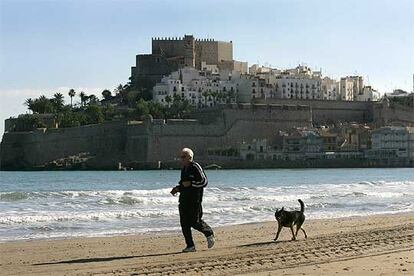 Un jubilado corre con su perro por la playa de Peñíscola.