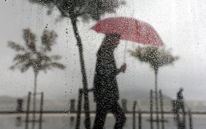 Una mujer camina bajo la lluvia en el paseo de la Concha de Donosti (Gipuzkoa).