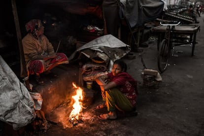 Dos mujeres se calientan en el fuego frente a sus casas en un área de asentamientos informales en el centro de la ciudad de Dacca. Más del 25% de la población de la ciudad vive en barrios de chabolas o asentamientos irregulares.