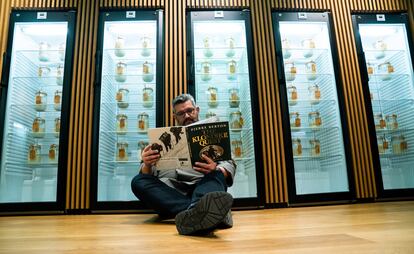 Karl De Smedt leyendo un libro en el suelo de su panadería, ante cientos de tarros con masas madres.