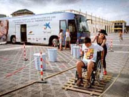Un chico comprueba las dificultades de quienes se mueven en silla de ruedas junto al autobús de la accesibilidad, en Valencia.