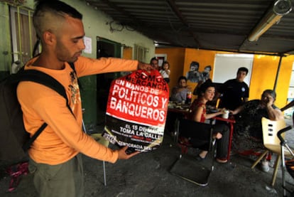 An activist shows a poster for the original May 15 demonstration as a shanty-dwelling family sits down to lunch in the background.