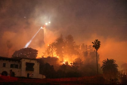 A helicopter performs a water drop, as smoke and flames rise from the Sunset Fire in the hills overlooking the Hollywood neighborhood of L.A. on January 8.