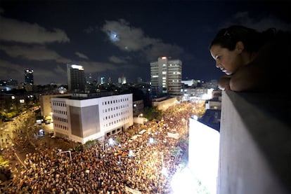 Una joven contempla desde una azotea a las centenares de personas que han marchado en Tel Aviv para protestar contra el aumento del coste de la vida.