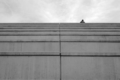 Un hombre con mascarilla sentado en las escaleras frente a la Torre Glòries (Barcelona, 2021).