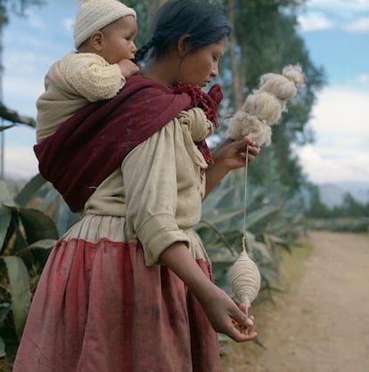 Mujer hilando con su bebé a la vera de un camino.