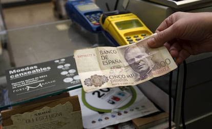 Un comerciante sostiene un billete de 5000 pesetas en un establecimiento.