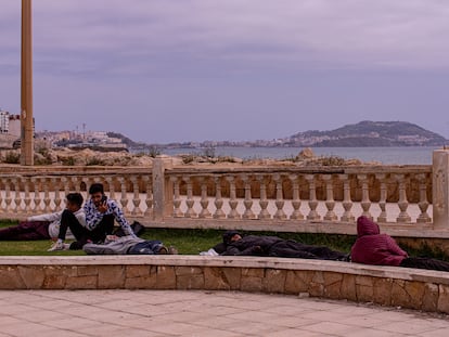 Varios jóvenes descansan en un jardín próximo al paseo marítimo de la ciudad de Castillejos (Fnideq en árabe), en Marruecos. Al fondo se observa la ciudad de Ceuta, el viernes.