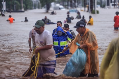 Personas cruzan una avenida inundada por el paso del huracán 'John' en la parte alta del puerto de Acapulco.