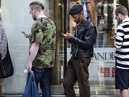 Tres jóvenes usan sus móviles mientras hacen cola para entrar en un establecimiento Uniqlo, en Nueva York.