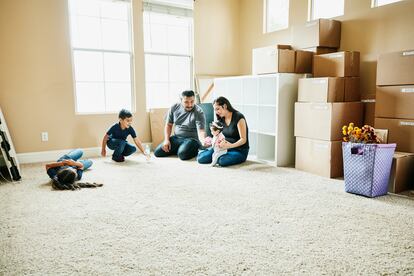 Familia sentada en el suelo de la sala de estar de una casa nueva durante el día de la mudanza.