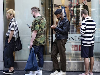 Tres jóvenes usan sus móviles mientras hacen cola para entrar en un establecimiento Uniqlo, en Nueva York.
