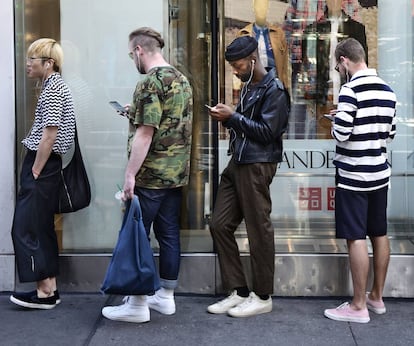 Tres jóvenes usan sus móviles mientras hacen cola para entrar en un establecimiento Uniqlo, en Nueva York.