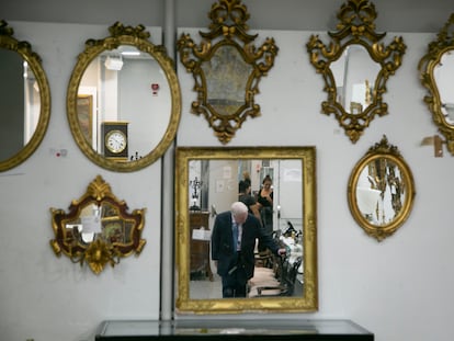 Un hombre que comprueba una silla que sale a subasta, reflejado en uno de los espejos exhibidos en la Sala Retiro, este miércoles.