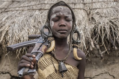 En una imagen culturalmente inusual pero cada vez más habitual, una niña de la tribu bodi del Parque Nacional de Mago posa con un Kalashnikov AK-47 y el arreo de reses como tocado improvisado. Las mujeres no poseen ni usan armas, pero cada vez es más frecuente que, a petición de los turistas, posen con ellas. Las tribus tienden a emular con cada grupo de visitantes aquello que creen que ha impresionado al grupo anterior y que por extensión les ha permitido ser fotografiados más veces y obtener más dinero por ello.