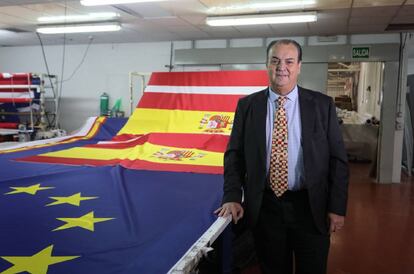 El empresario José Luis Sosa Dias, en su fábrica de banderas junto a insignias de España y de la Unión Europea.