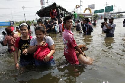 Personas evacuadas por las inundaciones abandonan el vehículo militar que les transportaba, bloqueado en la carretera en Bangkok