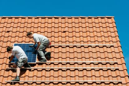 Dos instaladores fijan una placa solar en una vivienda recién construida en Países Bajos.