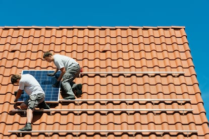 Dos instaladores fijan una placa solar en una vivienda recién construida en Países Bajos.