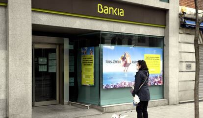 Una mujer pasea con un perro frente a una sucursal de Bankia un día después de que Banco Central Europeo (BCE) haya especificado que decidirá 
