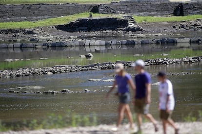 Tres personas caminan por el embalse de Portomarín, en Lugo, el 27 de julio. La escasez de agua ha hecho visibles los restos del antiguo pueblo.