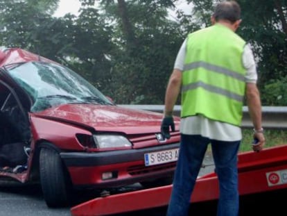 Un coche accidentado en una carretera de Asturias es recogido por una gr&uacute;a.