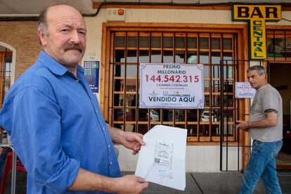 Ángel Iluminado Alonso muestra el boleto millonario ante su bar en Mayorga de Campos (Valladolid).