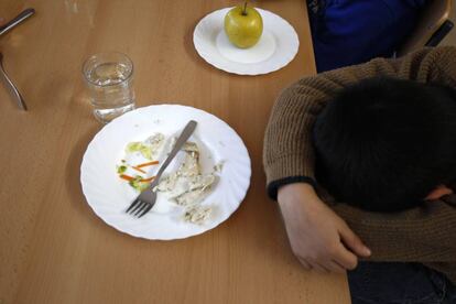 Los niños comen pescado en un comedor escolar.