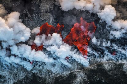 Huele a roca quemada y siento el calor del magma bajo mis pies mientras atravieso, a la luz de la luna, el parque nacional de los Volcanes de Hawái. Busco afloramientos de lava para fotografiarlos en el mejor momento, justo antes del amanecer.<p>Esta imagen de agosto de 2018 muestra el contraste del rojo intenso de la lava activa con el gris de la roca al enfriarse entre las nubes de vapor tóxico.</p>