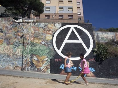 Dos niñas juegan ante un símbolo anarquista, la A de Can Franquesa, en un muro de Barcelona.