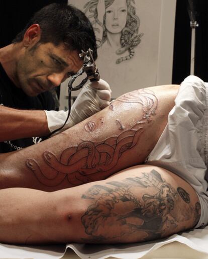 Uno de los artistas participantes en la convención tatúa la pierna a una cliente.