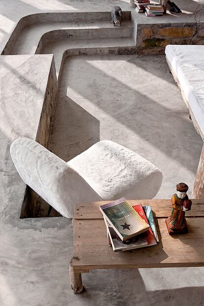 Rincón de lectura con escaleras de cemento que sirven de espacio para la convivencia. Mesa de madera y figura de porcelana. 