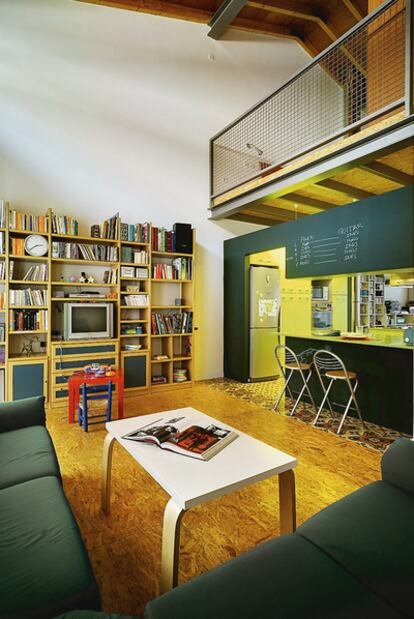 Desde el salón, con sofás verdes, a juego con la pizarra de la pared de la cocina, se ve la barandilla que da a la habitación principal.