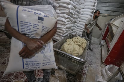 Un trabajador carga un saco de harina mientras se prepara la masa para la producción de pan en una panadería del Programa Mundial de Alimentos de Nacional Unidas, este jueves en Deir al Balah (Gaza)